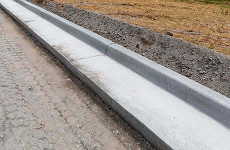 Concrete curb installation alongside a road under construction, showing a smooth finished curb and adjacent soil