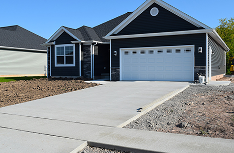 Newly poured concrete driveway in front of a modern residential home, with surrounding construction site