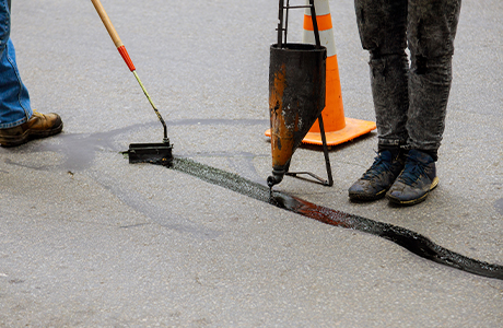 Workers Performing Crack Sealing on Asphalt Pavement Workers using crack sealing equipment to fill asphalt pavement cracks with sealant for road maintenance