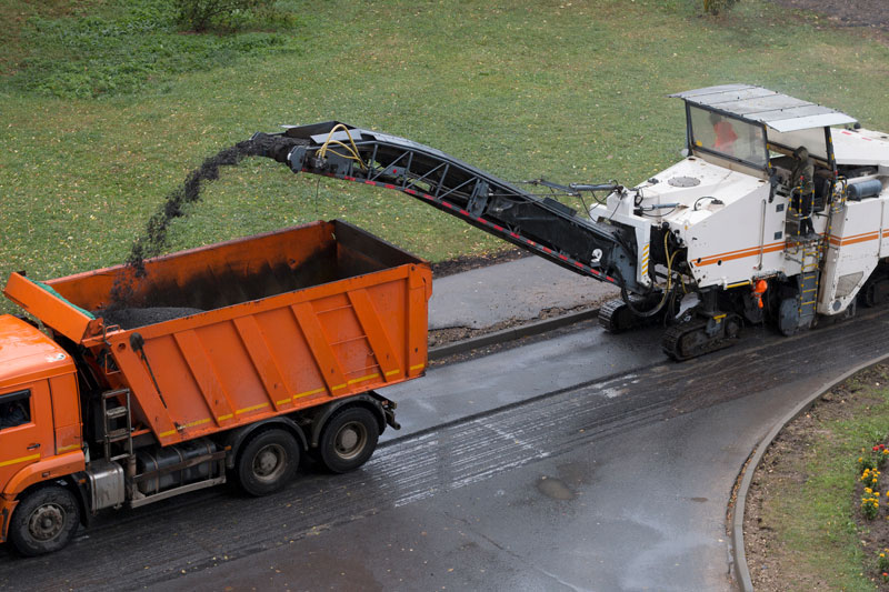 Asphalt Milling Machine Recycling Materials into Dump Truck Asphalt milling machine loading removed road materials into a dump truck for recycling during a roadway resurfacing project