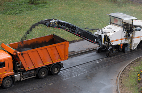 Asphalt milling machine loading removed road materials into a dump truck for recycling during a roadway resurfacing project