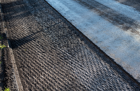 Close-up of asphalt milling process removing the surface layer of the road, showing textured grooves and prepared surface for repaving