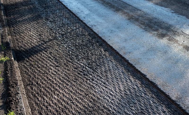 Asphalt Milling Process to Remove Surface Layer Close-up of asphalt milling process removing the surface layer of the road, showing textured grooves and prepared surface for repaving